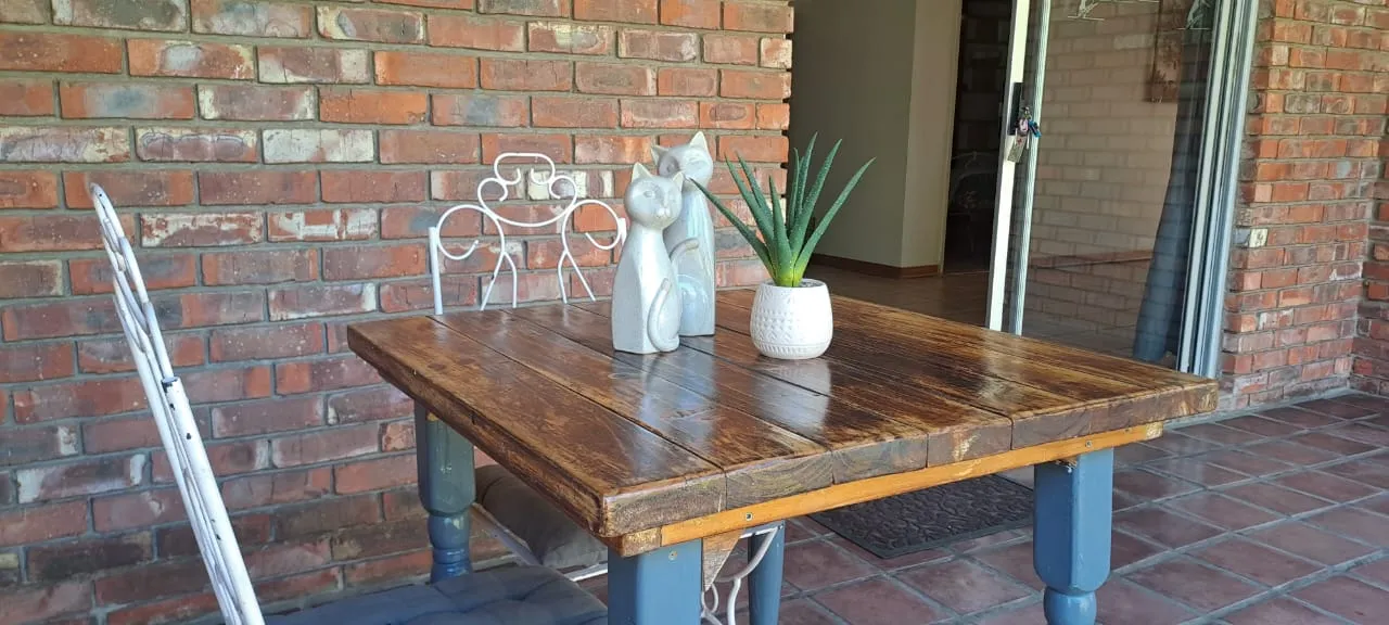 Rustic wooden dining table with potted aloe and decorative cat ornaments on a tiled patio at Bloom Guest House in Dan Pienaar, Bloemfontein.